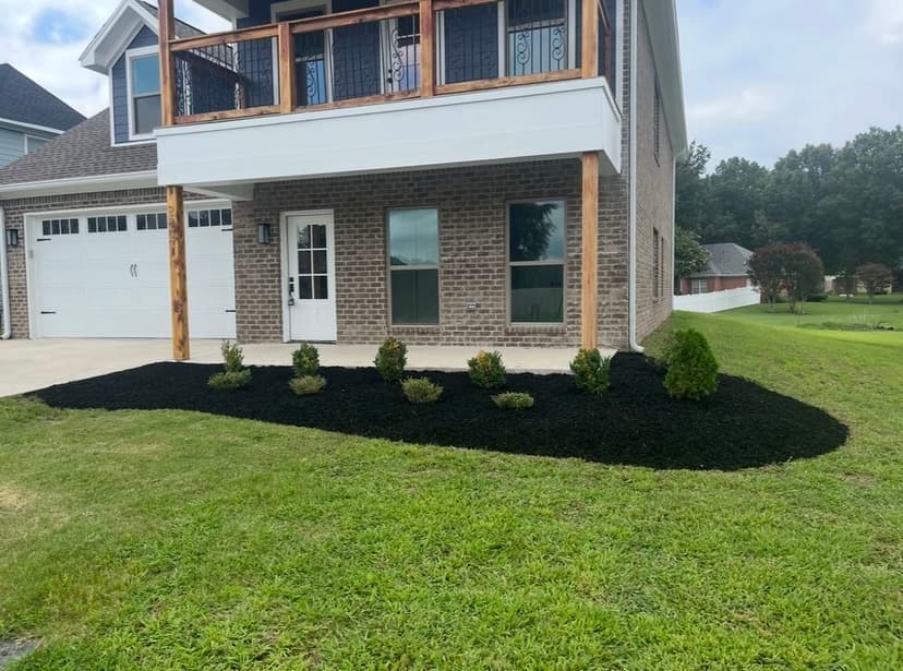Newly landscaped front yard featuring black mulch and small shrubs around a modern home.