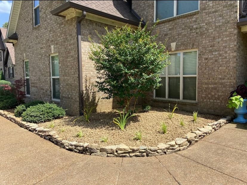 Lush landscape design featuring a flowering shrub and stone-bordered garden beds.