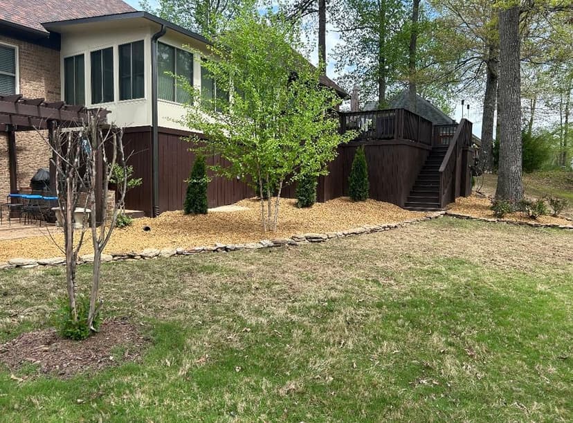Backyard landscape with wooden deck, gravel pathway, and newly planted trees.