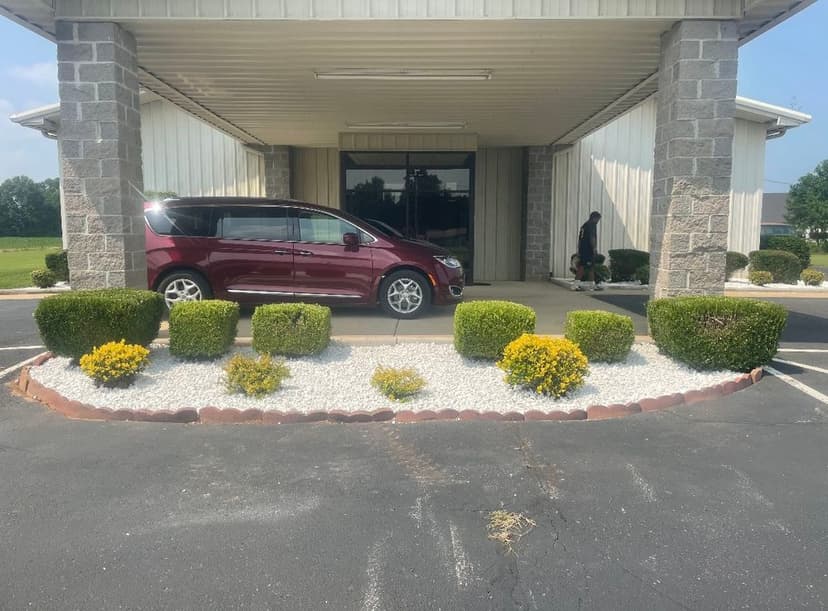 Maroon minivan parked in front of a commercial building with manicured shrubs and white gravel.