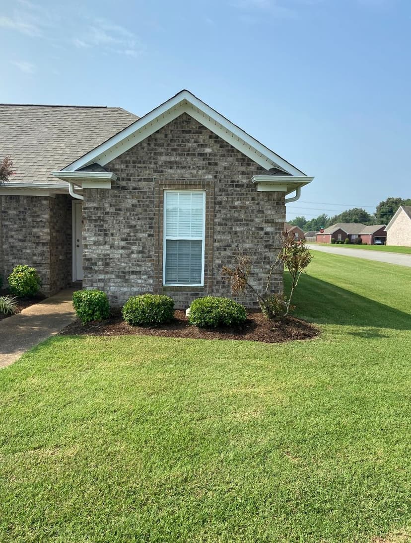 Brick house exterior with landscaped yard and clear sky, showcasing curb appeal.