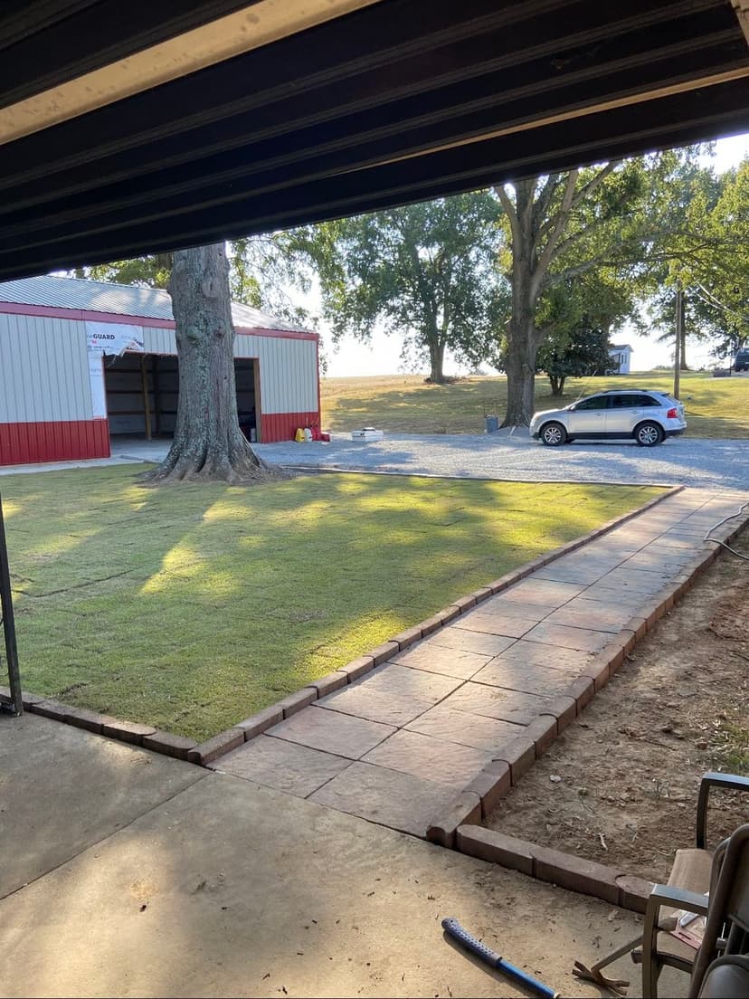 View of a landscaped yard with a stone path, garage, and parked car under a tree.
