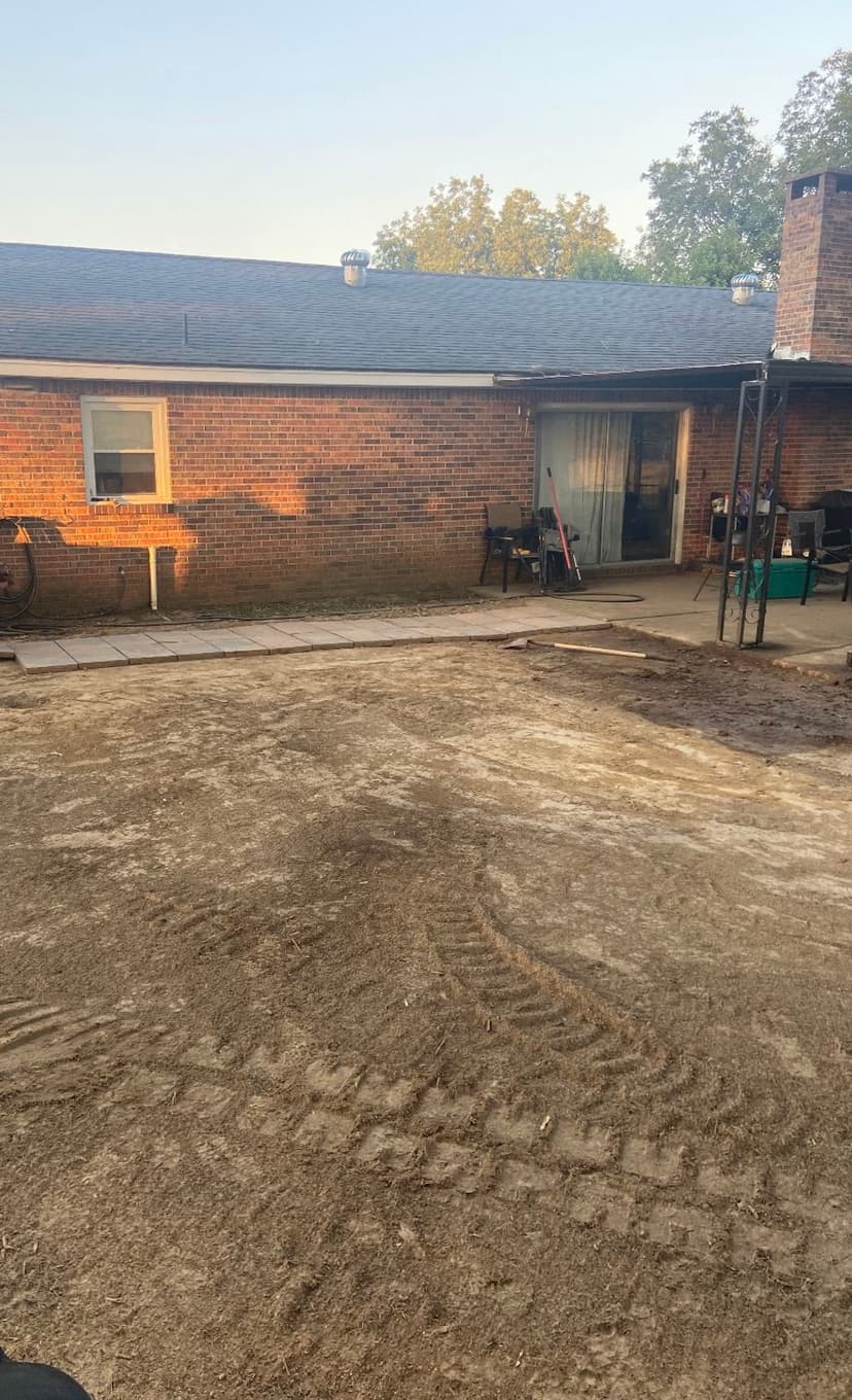 Backyard renovation showing dirt patch and brick house with clear sky and trees.